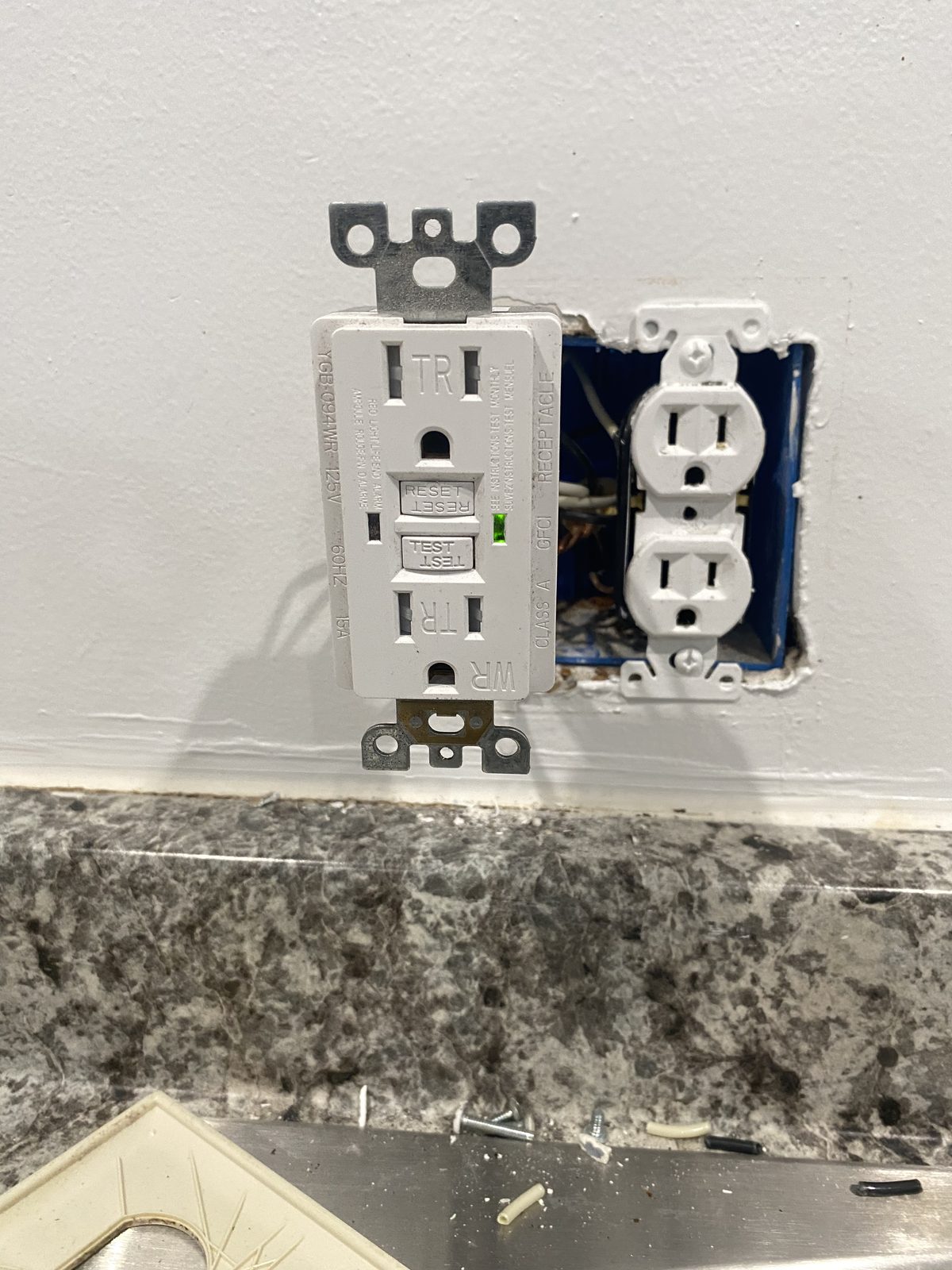 New GFCI outlet with green status light installed next to an older outlet
